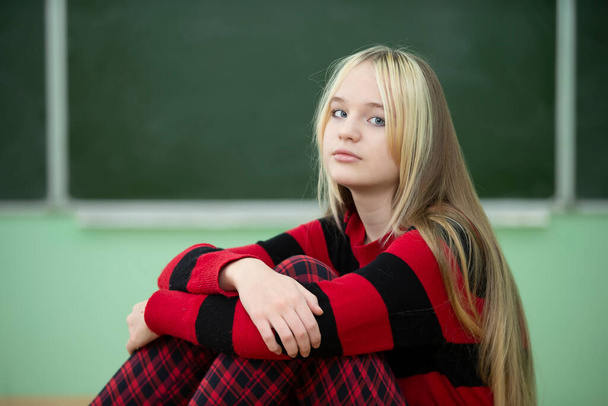 Lukioikäinen teini. Teini-ikäinen tyttö istuu liitutaulun taustalla ja katsoo kameraa. - Valokuva, kuva