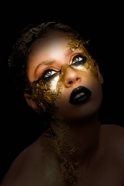 Fashion art Golden skin. Model girl with festive golden glamorous shiny professional make-up. Gold jewelry, bijouterie, accessories. Beautiful golden metallic body, black lips and skin. - Foto, afbeelding