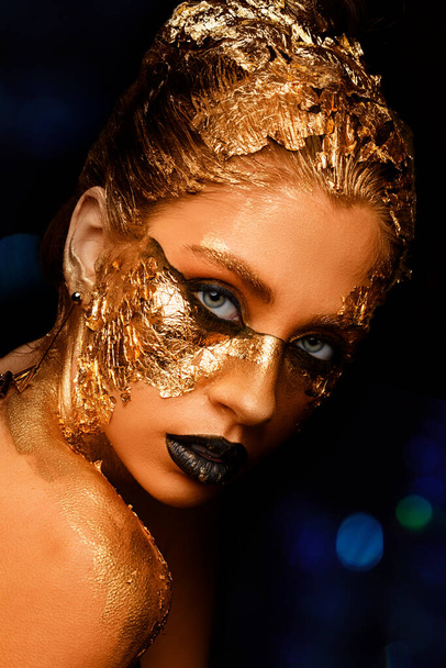 Fashion art Golden skin. Model girl with festive golden glamorous shiny professional make-up. Gold jewelry, bijouterie, accessories. Beautiful golden metallic body, black lips and skin. - Foto, Imagen