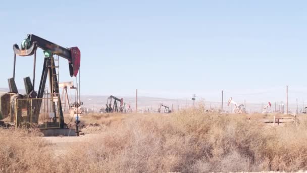 Pozos con tomas de bomba en el campo petrolífero, California, EE.UU. Aparejos para la extracción de fósiles crudos que trabajan en yacimientos petrolíferos. Paisaje industrial, derricks en valle del desierto. Muchas plataformas de calabazas en pozos de petróleo de bombeo. - Metraje, vídeo