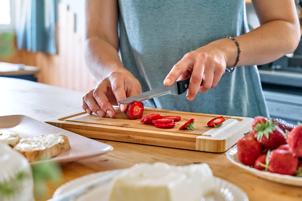 Mujer haciendo sándwich de fresa de verano. Las manos femeninas cortan fresa roja madura en la tabla de cortar. Comida saludable, almuerzo a dieta de frutas. - Foto, Imagen