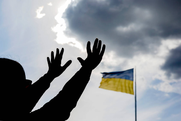 Handen omhoog tegen de achtergrond van de vlag van Oekraïne. Gebed voor hulp en zegeningen voor het land Oekraïne. Bescherming van de natie. - Foto, afbeelding