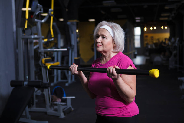 Уверенная в себе здоровая пожилая женщина, тренирующаяся в тренажерном зале, делающая бицепсы - Фото, изображение