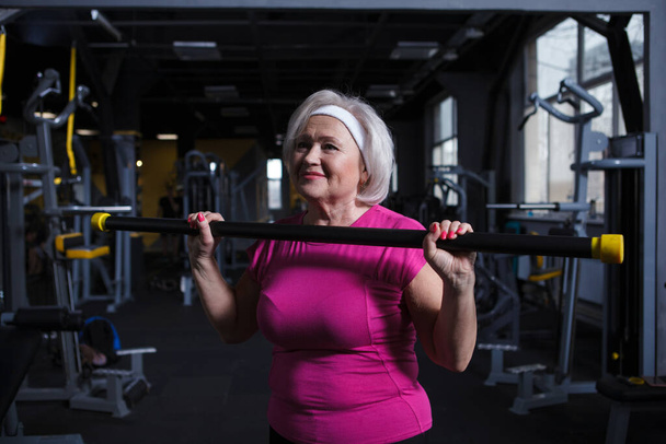 Happy healthy senior woman exercising with bodybar at the gym - 写真・画像