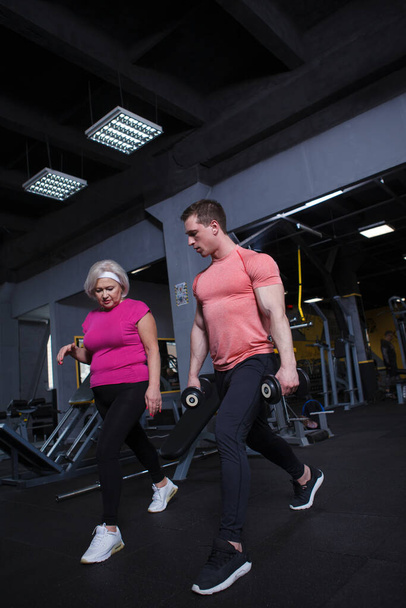 Full length πλάνο μιας ηλικιωμένης γυναίκας που μαθαίνει lunges άσκηση με προσωπικό γυμναστή στο γυμναστήριο - Φωτογραφία, εικόνα