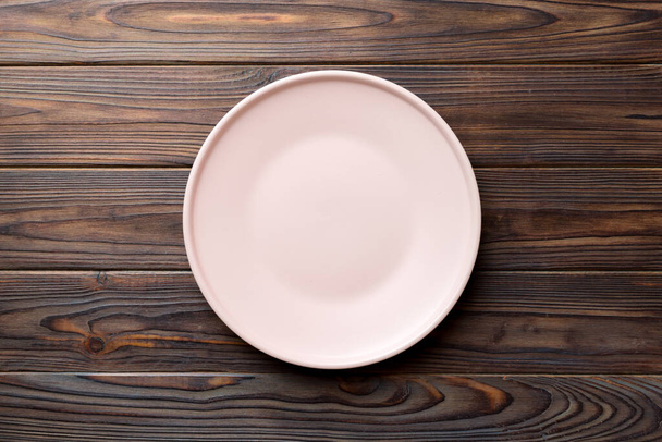 Horní pohled na prázdný růžový talíř na dřevěném pozadí. Prázdné místo pro váš design. - Fotografie, Obrázek