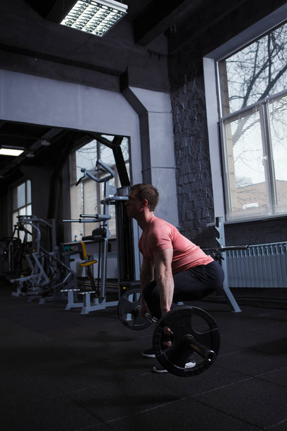 Вертикальный кадр мускулистого спортсмена, делающего упражнения на тягу с штангой - Фото, изображение