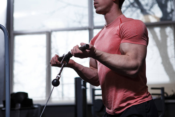 Recortado tiro de un musculoso culturista haciendo rizos bíceps en cable crossover máquina de gimnasio - Foto, imagen