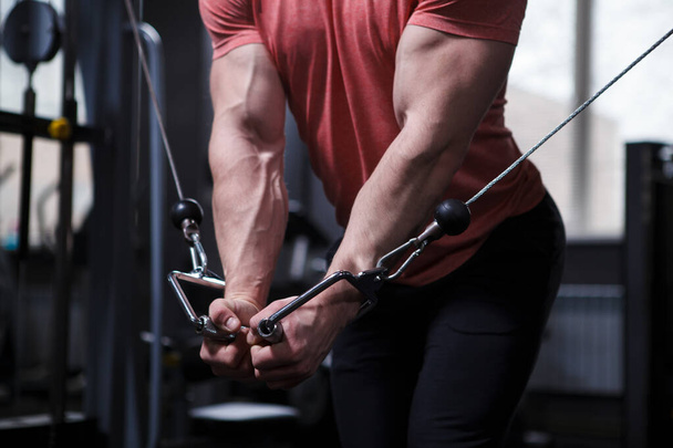 Περικοπή κοντά των μυών χέρια του bodybuilder άσκηση σε καλώδιο crossover γυμναστήριο μηχάνημα - Φωτογραφία, εικόνα