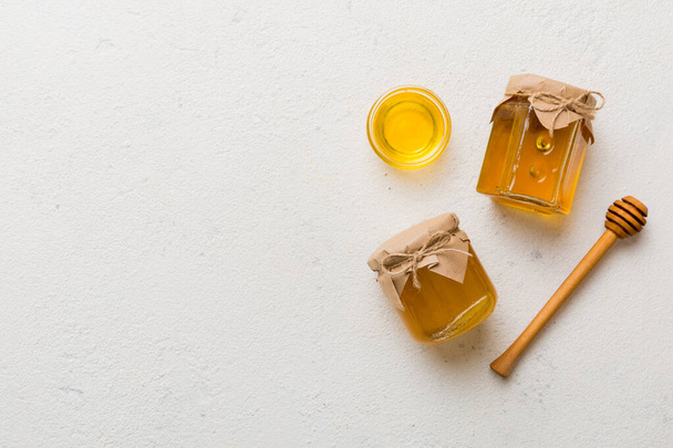 Glazen pot honing met houten motregen op gekleurde achtergrond. Honingpot en dipper hoog boven. Bovenaanzicht kopieerruimte. - Foto, afbeelding