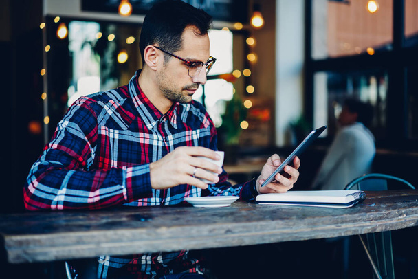 Millennial man in trendy eyewear reading news on websites via high speed 4G internet connected to digital tablet - Foto, Imagem