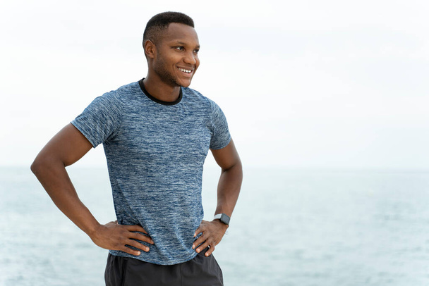Taille omhoog portret van de knappe fitness multiraciale man aan het strand staan in ontspannen houding en weg te kijken. Voorraadfoto  - Foto, afbeelding