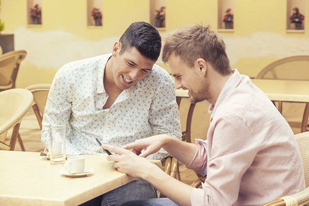 Two men sitting at cafe looking at tablet and smiling - Foto, Bild