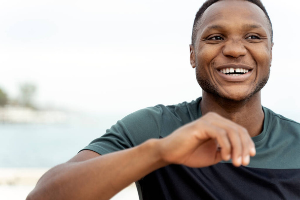 Vista del retrato del hombre afroamericano riendo en voz alta mientras estaba de pie a la orilla del mar y preparándose para el trote. Foto de stock - Foto, imagen