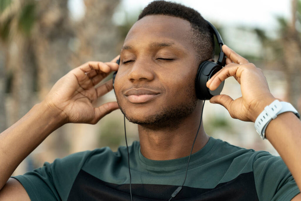 Harmonia z naturą. Sportowiec mężczyzna cieszy się latem i słucha przyjemnej muzyki na słuchawkach z zamkniętymi oczami. Podróże, letnie wakacje na świeżym powietrzu - Zdjęcie, obraz