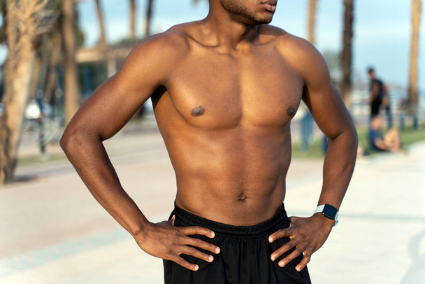 リラックスしたポーズで立っている間、夏の日にビーチで太陽を楽しんでハンサムなフィットネス多人種の男のクロップビュー。ストックフォト  - 写真・画像