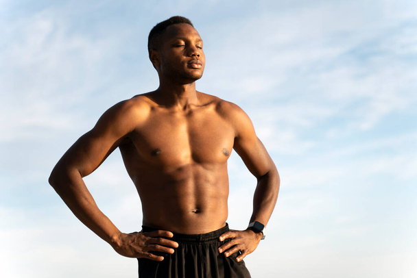 Young african american muscular guy in black beach shorts sunbathing at bright beach. Beautiful summer weather. Stock photo  - Photo, Image