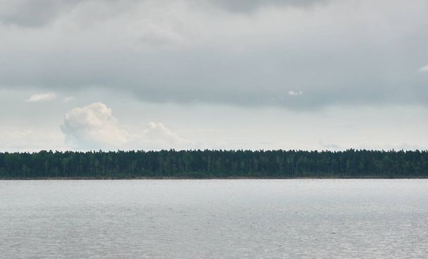 Панорамный вид с берега кристально чистого лесного озера (реки). Драматическое небо, светящиеся грозовые тучи. Идиллический пейзаж. Весна, раннее лето. Природа, окружающая среда, экология, экотуризм, походы - Фото, изображение