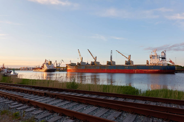 Großes Frachtschiff wird im Hafenterminal verladen. Sonnenuntergang. Blick von der Bahn. Güterverkehr, Seeschiff, Logistik, globale Kommunikation, weltweite Schifffahrt, Wirtschaft, Industrie - Foto, Bild