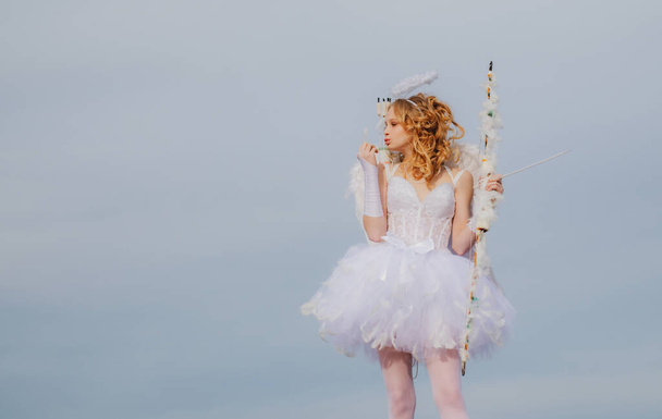 Angel teen with arrow and wings. Charming curly little girl in white dress and wings - angel cupid girl. St Valentines day. Space for text. Postcard for Valentines Day. - Фото, зображення