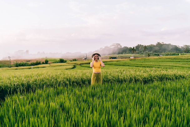 Cheerful young lady in summer clothes enjoying lush exotic nature while taking stroll about green rice fields in Bali countryside during summer vacation - Foto, immagini