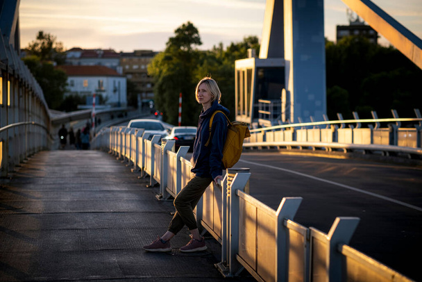 Una femmina con uno zaino giallo si trova su un ponte di metallo durante il tramonto. Oporto, Portogallo. - Foto, immagini