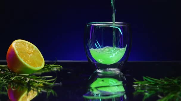 Κοντινό πλάνο του ρίχνει πράσινο ποτό κοκτέιλ σε ένα διαφανές ποτήρι στέκεται στον πάγκο μπαρ. Κλιπ μετοχών. Bar counter διακοσμημένο με πράσινα φύλλα και πορτοκαλί - Πλάνα, βίντεο