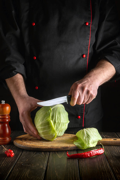 シェフは新鮮な野菜とヴィンテージキッチンテーブルのサラダ用ナイフで新鮮なキャベツをカットします。 - 写真・画像