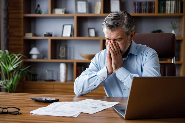 Depressed adult man calculating monthly expenses. Mad gray-haired businessman feels frustrated about high bills, bank debt, tax invoice, credit payment. Financial problems, crisis, bankruptcy - Foto, imagen