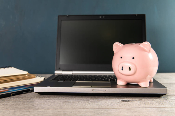 Piggy bank with laptop on working table - Фото, зображення