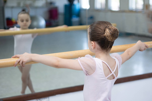 Χαριτωμένο κοριτσάκι μπαλαρίνα σε απαλό ροζ tutu και παπούτσια μπαλέτου εξάσκηση χορευτικές κινήσεις. Η μικρή σπουδάζει μπαλέτο. Αντιγραφή χώρου. - Φωτογραφία, εικόνα