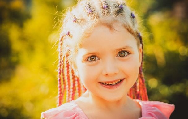 Child girl with stylish hair rope dreadlocks. Kid with fashionable hairstyle on blur background outdoor. Children beauty and fashion - Фото, изображение
