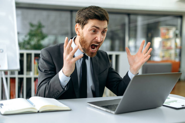 Irritado chocado caucasiano masculino, trabalhador de escritório, gerente de produto, irritado gritando com um laptop durante o trabalho, sentar em um escritório moderno, em trajes de negócios, frustrado com a interrupção de um importante negócio - Foto, Imagem