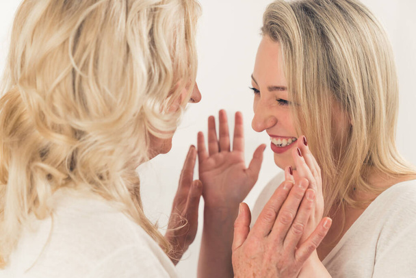 Close-up studio shot of two women with blonde hair and big smiles, standing close, touching their hands and laughing. High quality photo - Photo, image