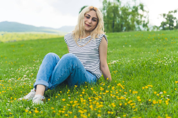 Çimlerin üzerinde kameraya gülümseyen güzel sarışın beyaz kız. Park arka planı tam çekim yaz konsepti. Yüksek kalite fotoğraf - Fotoğraf, Görsel