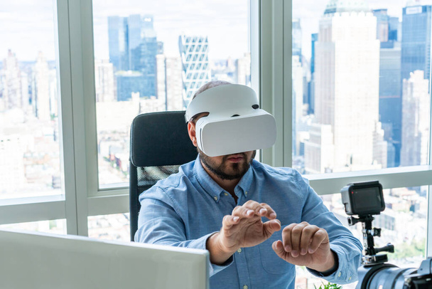 From above of man in formal shirt showing virtual reality glasses to camera while sitting near window view of modern city - Foto, Bild
