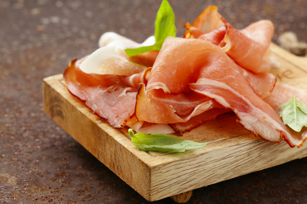 Smoked ham jamon (Parma) with basil leaves on a wooden board - Photo, Image