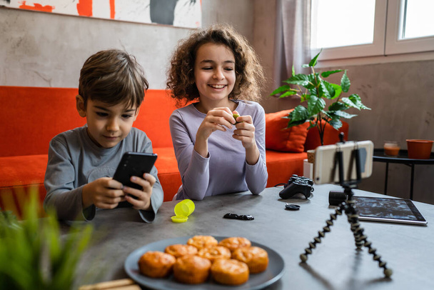 Erkek ve kız kardeş iki kardeş cep telefonuyla video blogu yapıyorlar evlerinden internet günlüğü için en sevdikleri oyuncak eleştirisi hakkında sosyal ağ kopyalama alanı için içerik oluştur ve paylaş - Fotoğraf, Görsel