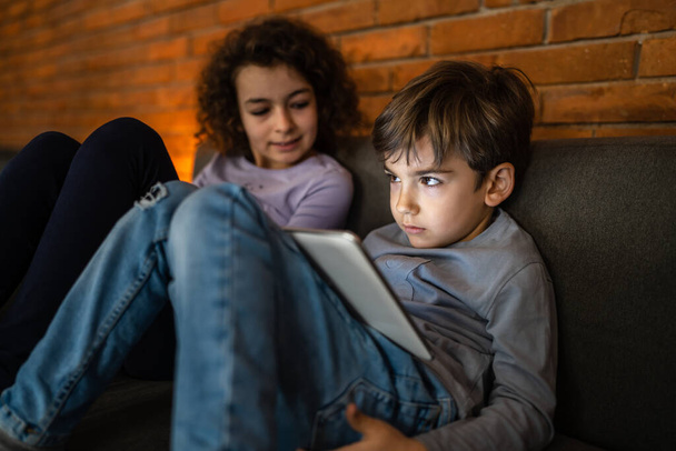 Kleine blanke jongen zitten door zijn zus met behulp van digitale tablet thuis - Foto, afbeelding