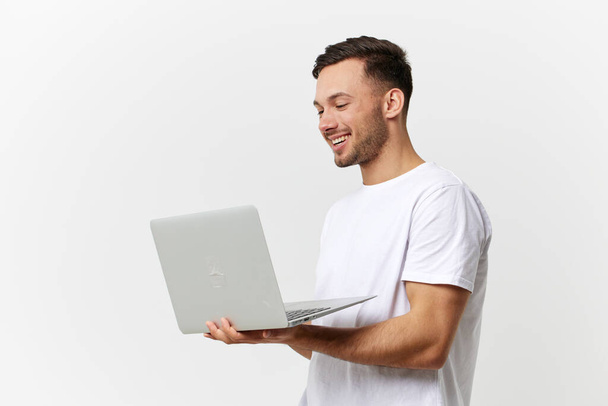 Happy passionate enjoyed tanned handsome man in basic t-shirt chatting with friends by laptop posing isolated on over white studio background. Copy space Banner Mockup. Gadgets lifestyle concept - Photo, Image