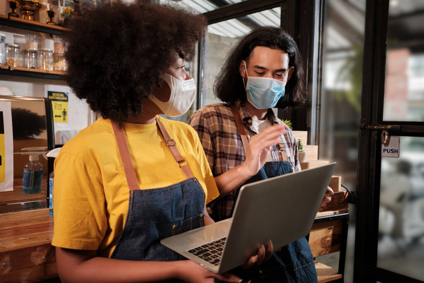 Two young cafe barista partners and entrepreneur work with face mask in coffee shop, waiting for customers order in new normal lifestyle service, SME business impact from COVID19 pandemic quarantine. - Foto, Imagen