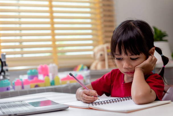 Little Asian girl sitting alone and looking out with a bored face, Preschool child laying head down on the table with sad bored with homework, spoiled child - Фото, зображення