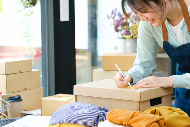 Young Asian businesswoman Start up small business owner online store writing customers address in shipping box. - Photo, image