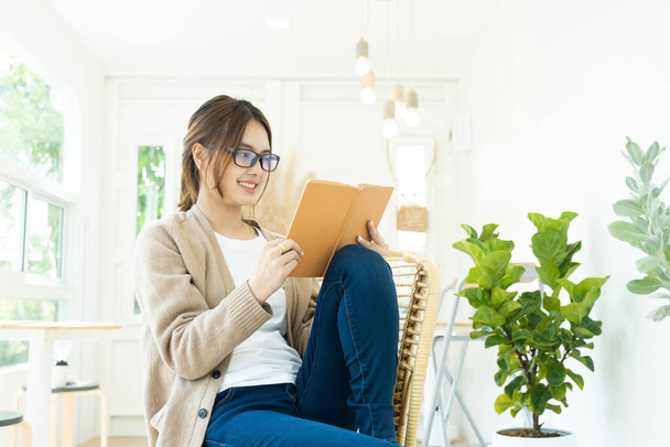 Nuori naispuolinen opiskelija, joka lukee tuolilla istuvaa kirjaa, opiskelee verkossa tai opiskelee itsekseen. - Valokuva, kuva