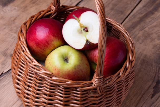 Fresh red apples in basket over wooden background - 写真・画像