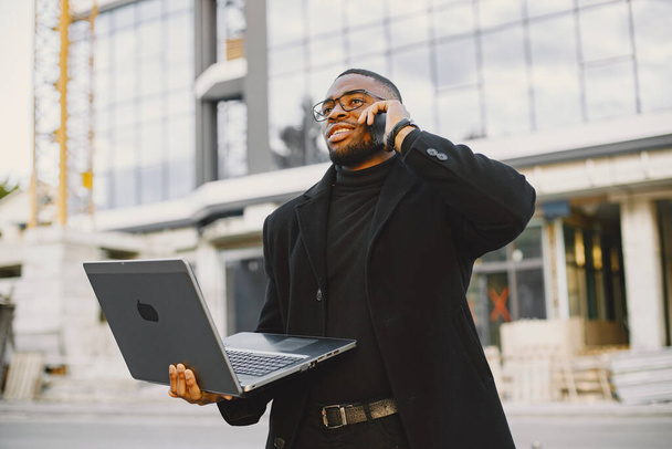 Young black businessman working with laptop. Standing near glass building. - Fotó, kép