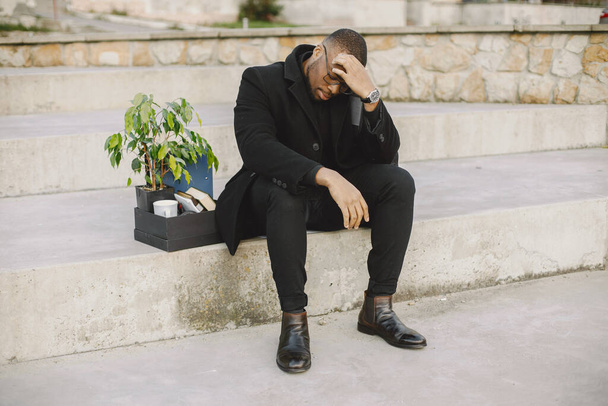 Employee get fired. Black man sitting with box on stairs and regretting. - Photo, Image