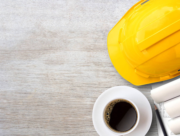 Желтый шлем безопасности или каска и строительная бумага планы на фоне деревянного стола. Идея бизнес-строительства, концепция строительной отрасли. Вид сверху с пространством для копирования для вашего использования. - Фото, изображение