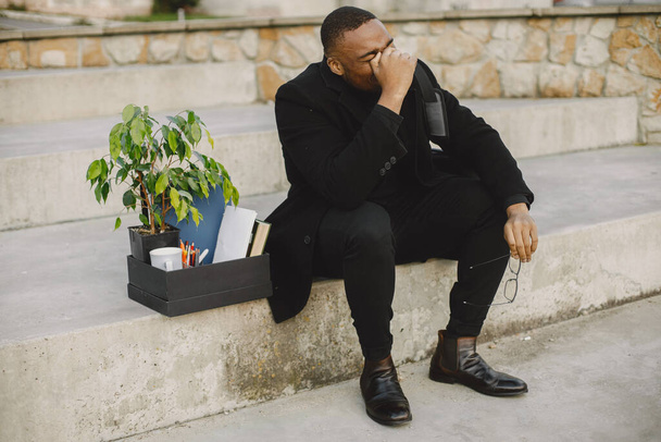 Employee get fired. Black man sitting with box on stairs and regretting. - Fotografie, Obrázek