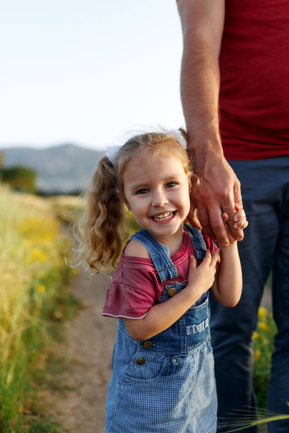 Little girl holding fathers hand,looking camera,smiling.Happy family, bonding, love. Summertime. Dad and daughter. Fathers day. - Photo, Image